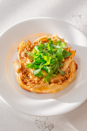 Golden layered lasagna arranged in a ring, topped with fresh green arugula leavesの写真素材