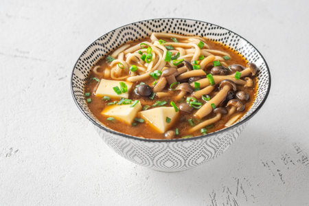 Warm noodle soup features silky tofu, earthy mushrooms, and scallions in savory baseの写真素材