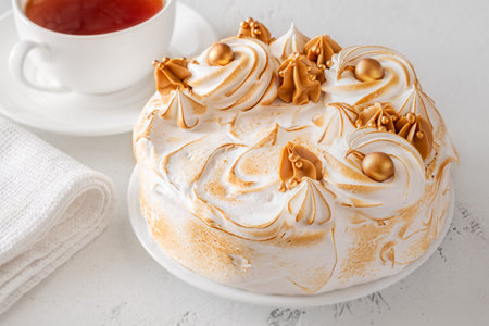 Luxurious Medovik cake with torched meringue served beside tea on white background