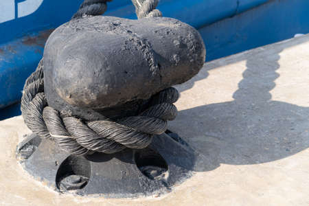 Mooring bollard on a background of blue water surface, loaf embankment, cast-iron chain