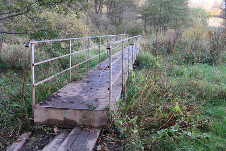 Pedestrian metal bridge over a small river, autumnの写真素材