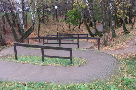 Winding walking path in the park, lined with tiles, wooden railing, fallen leaves, autumnの写真素材