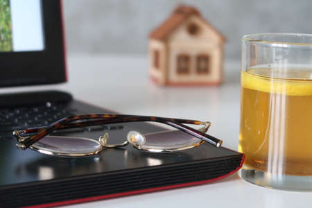 Glasses lie on the laptop keyboard, next to a glass of tea, in the background a toy house, a symbol...