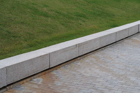 White-tiled walkway, stone curb and hillside lawn