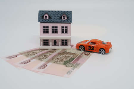 A toy house and a car stand on 100 ruble banknotes, own housing and a car, a symbol of prosperity