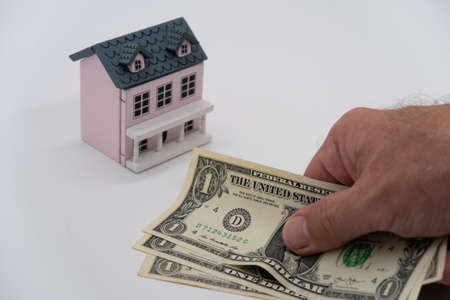 A man hand holds a bundle of American banknotes, a toy house is a symbol of mortgage and real estate purchase next to it, moneyの写真素材