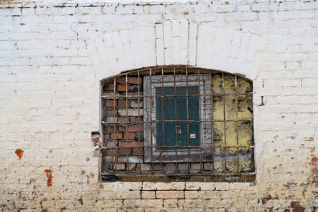 Old vaulted window with brick wall with metal grate and wooden frame, white paint peeling on the wallの写真素材