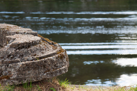 Old destroyed concrete structure overgrown with moss and lichen on the river bank against the background of the water surfaceの写真素材