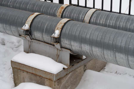 Two pipes of the heating system are fastened with metal clamps to a concrete support.の写真素材