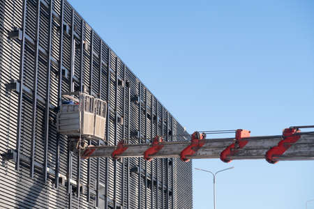 Telescopic boom of a construction truck crane with a cradle on the facade of a building, repair work, background.の写真素材