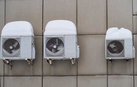 Two large and one small air conditioner covered with snow from above and inside, background