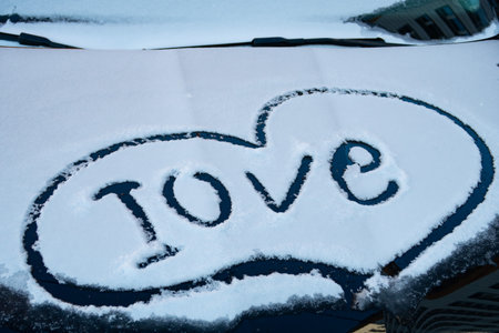 There is a layer of snow on the hood of the car, on it the inscription Love, moodの写真素材