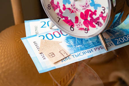 A clock and a cardboard house on Russian banknotes symbolize the time of mortgage paymentsの写真素材