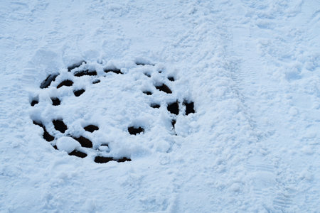 Metal manhole cover with holes and melted snow on the carriageway, winter snow backgroundの写真素材