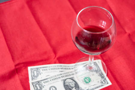 An unfinished glass of wine and a couple of american dollars on a red tablecloth