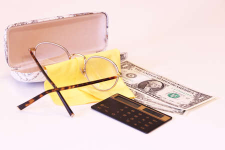 A case with glasses lies on the table, there are several dollar bills and a calculator, financial experienceの写真素材