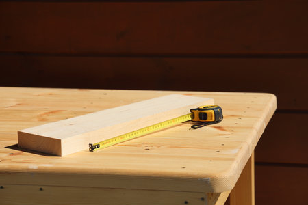 On the light surface of a wooden table there is a scrap of a board and a tape measure for carpentry...