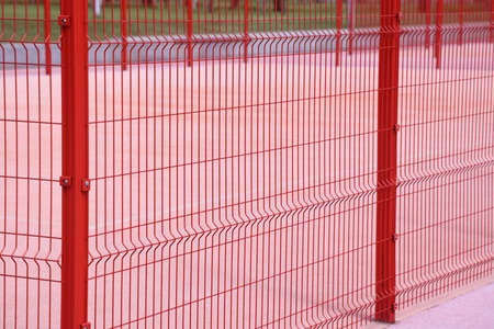 View of a new sports field with a pink cover through a red wire fence, pink backgroundの写真素材