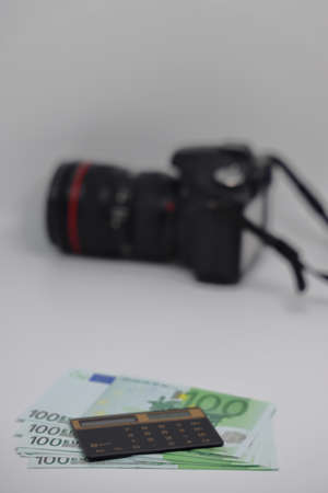 The calculator lies on one hundred euro banknotes against the background of a camera, earnings on...