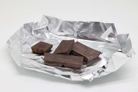 Pieces of chocolate on silver foil, sweet treat, sweet edible background