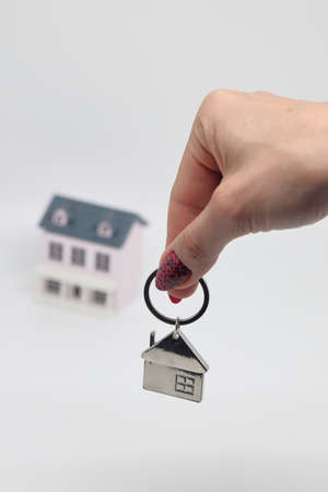 A female hand holds a keychain in the shape of a house on the background of a toy house, mortgage, real estateの写真素材