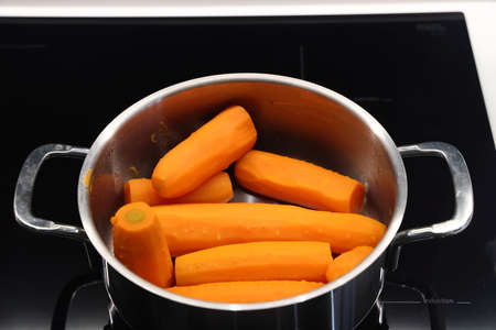 Boiled carrots in a metal pan, cooking on an electric stoveの写真素材
