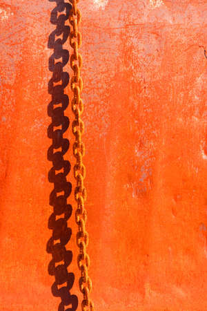 Shadow of a rusty metal chain on a rusty steel surface, reddish background.の写真素材