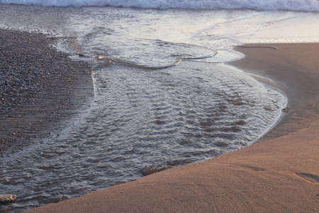 Stream flows into the sea, sandy shore and jackdaw, evening illumination.の写真素材