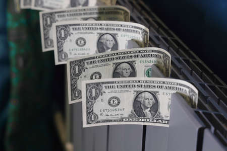 Dollar bills are inserted into the slots of the heating radiator, the rise in the cost of heat, the fuel crisis.の写真素材