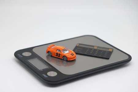 A toy car and banknotes lie on a kitchen electronic scale next to a calculator, the cost of operating a car.の写真素材