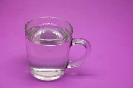 Transparent glass tumbler with water on a purple background. Copy space