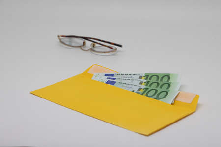 Glasses. banknotes in a yellow envelope. open envelope with banknotes on a light background. envelope with banknotes. close-up of an envelope with cash. international currency banknote. Euro dollars rublesの写真素材