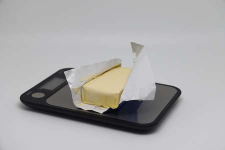 A piece of butter in a package on a white background, proper nutrition, calorie counting. kitchen scalesの写真素材