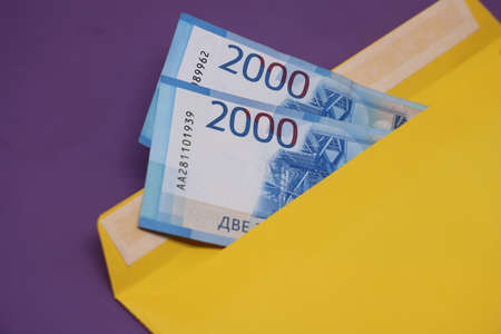 Banknotes in a yellow envelope on a purple background. Briber concept. Salary in envelopes. financial fraud. close upの写真素材