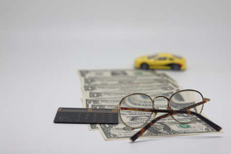 Track of dollar bills. Toy car on a white background with glasses and a calculator, the concept of car ownership cost autocreditの写真素材