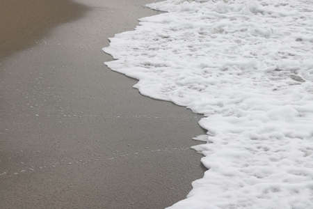 Foamy wave on the background of sandy sand, wet beach sand