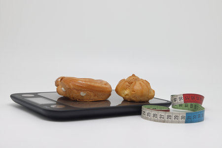 Cakes and pastries with cream lie on electronic kitchen scales, calorie counting and weight control,...