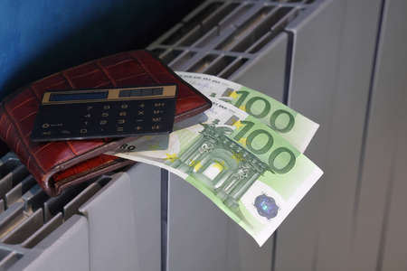 Calculator, wallet and banknotes with 100 euros lie on the radiator of the heating system, the cost...