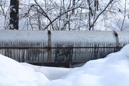 The main provides the city with hot water. selective focus. The large pipes of the central heating system are covered with snow. Icicles on pipes. fuel crisis. Increasing the cost of heatingの写真素材
