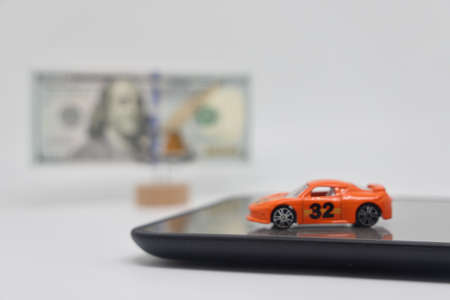 A toy car stands on an electronic scale next to a stand with a banknote, the concept of determining the cost of a car when selling, car insurance and car loansの写真素材