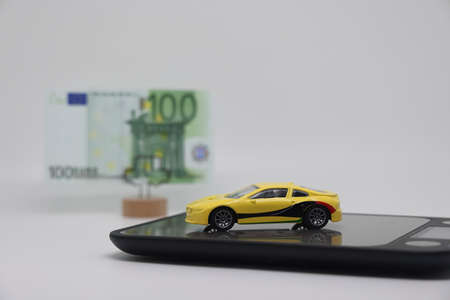 A toy car stands on an electronic scale next to a stand with a banknote, the concept of determining the cost of a car when selling, car insurance and car loansの写真素材