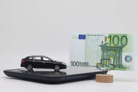 A toy car stands on an electronic scale next to a stand with a banknote, the concept of determining the cost of a car when selling, car insurance and car loansの写真素材