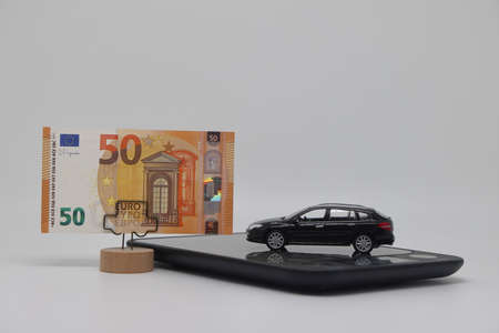A toy car stands on an electronic scale next to a stand with a banknote, the concept of determining the cost of a car when selling, car insurance and car loansの写真素材