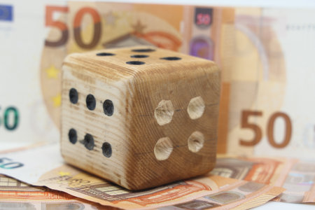 A homemade play cube lays on a track of bills, symbolizes the volatility of financial marketsの写真素材