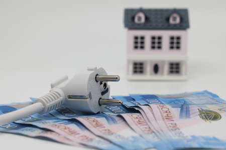 White electric cable and banknotes against the background of a toy model house, expensive electricity, saving electricityの写真素材