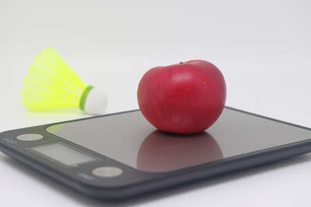 An apple on a kitchen scale against a background of a shuttlecock. Calorie counting. diet and sportsの写真素材