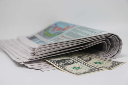 A rolled up stack of newspapers, banknotes stuck between the newspapers, news