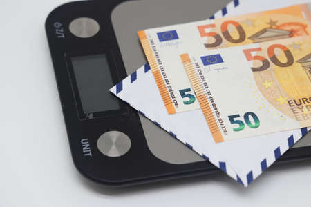 Banknotes in an envelope lie on a kitchen scale on a white background, financial strategies,...