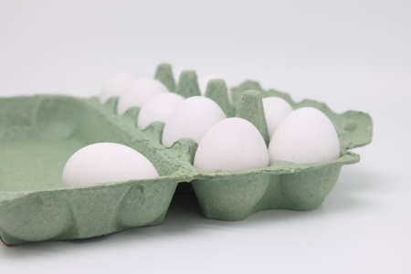 White chicken eggs lie in a cardboard tray on a white background
