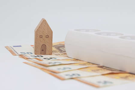 A white electric cable lies on banknotes against the backdrop of a house, expensive electricity,...